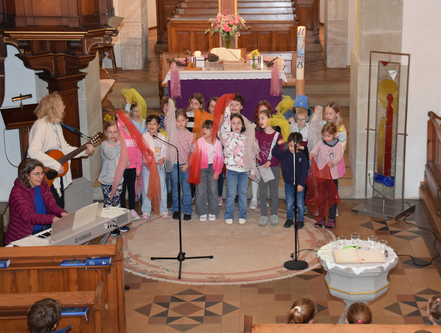 Foto mit Kindern vor dem Altar, alle wedeln mit bunten Tüchern